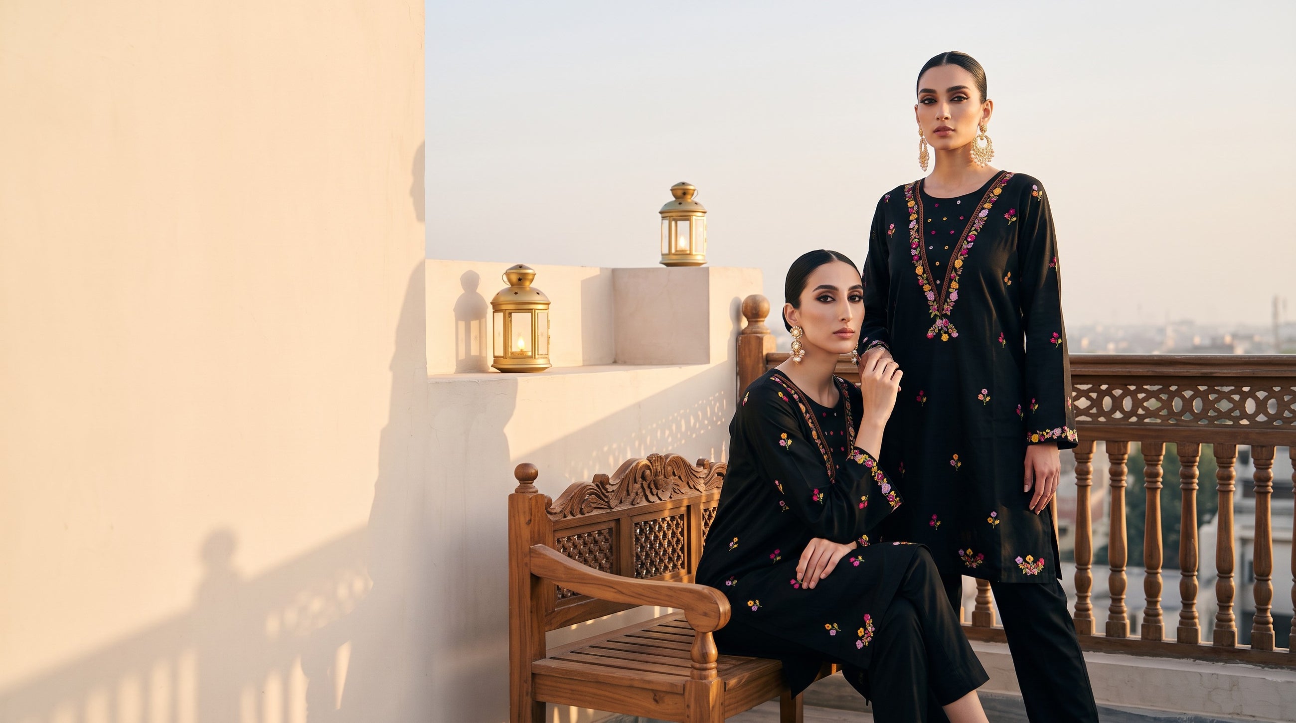 Two models in black embroidered kurtas on a rooftop terrace at golden hour