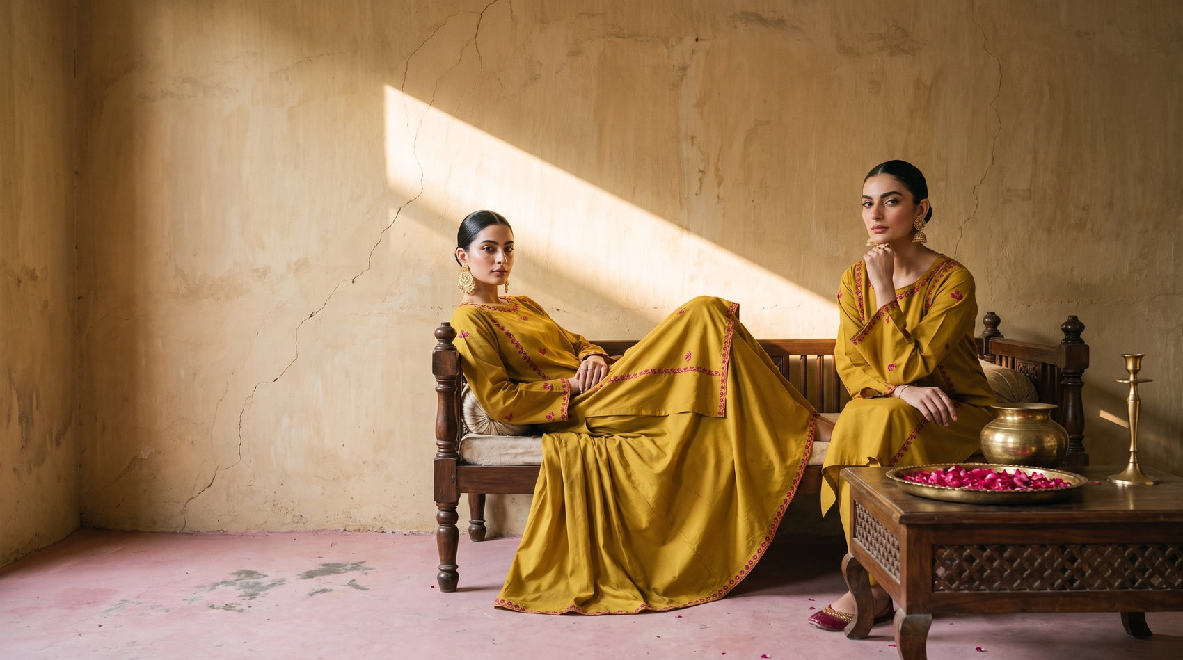 Two models in the mustard embroidered kurta set on a carved daybed in an ochre room
